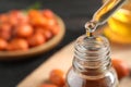 Dripping jojoba oil from pipette into bottle on background, closeup. Space for text