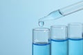 Dripping reagent into test tube on blue background, closeup. Laboratory analysis