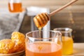 Dripping tasty honey from dipper into glass on table, closeup