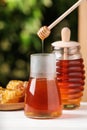 Dripping tasty honey from dipper into jar on white table