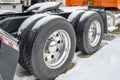 Drive axels of orange big rig semi truck with double wheels and tires on the winding parking lot with snow and ice Royalty Free Stock Photo
