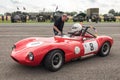Driver in classic vintage racing car in paddock talking to team mate