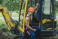 Driver concept. Excavator driver on construction site. Man driver at digger cabin. Muscular driver in working uniform