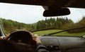 Driver driving a modern off road left hand drive LHD car on the mountain green forest country road at rainy moody day. POV inside Royalty Free Stock Photo