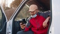 Driver with face mask under the chin using smartphone