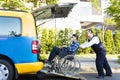 Driver helping man on wheelchair getting into taxi