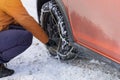 Driver installs chains on the wheel of his orange car in winter. Vehicle equipment for off-road. Royalty Free Stock Photo