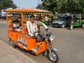 Driver of orange battery operated electric auto rikshaw waiting for passengers