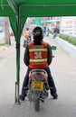 The driver in orange waistcoat sit on his motorcycle taxi, waiting for passenger.