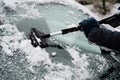 Driver is removing snow from car windshield with ice scraper and broom, clean car window from icy frost, winter season