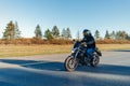 Driver riding motorcycle on empty road in beautiful autumn forest. Royalty Free Stock Photo