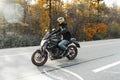 Driver riding motorcycle on empty road in beautiful autumn forest. Royalty Free Stock Photo