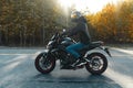 Driver riding motorcycle on empty road in beautiful autumn forest. Royalty Free Stock Photo