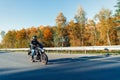 Driver riding motorcycle on empty road in beautiful autumn forest. Royalty Free Stock Photo