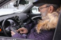 A driver is sitting in the car and looks at the mobile phone. Cold weather, snow-covered trees in the winter forest Royalty Free Stock Photo