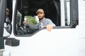 A driver sitting inside the semi-truck while looking through the open window with multiple trucks parked in the