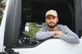 A driver sitting inside the semi-truck while looking through the open window with multiple trucks parked in the