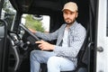 A driver sitting inside the semi-truck while looking through the open window with multiple trucks parked in the