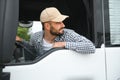 A driver sitting inside the semi-truck while looking through the open window with multiple trucks parked in the