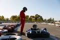 Driver wearing racing overalls and helmet standing nearby kart race car