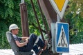 The driver in a white helmet and overalls is in the open cab of a crane and controls an arrow with a suspended load. A crane