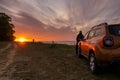 Driver, woman standing next to the Dacia Duster SUV admiring the beautiful sunset over the sea