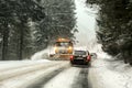 Driving on forest road through snowstorm, orange maintenance plough truck coming opposite way, view from car behind Royalty Free Stock Photo