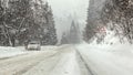Driving through heavy snowstorm blizzard at forest road, warning curves ahead sign right, and anonymous man with his car stopped Royalty Free Stock Photo