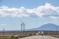Driving on a long straight road with heat shimmer toward mountains - wind turbines on one side and signs that say Gusty Winds Area Royalty Free Stock Photo