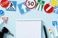 Driving school exam concept. Blank paper notebook, pen, road signs and traffic symbols on color background Royalty Free Stock Photo