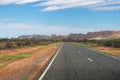 Driving towards the MacDonnell ranges. Empty road, no cars. Typical yellow Australian road signs. Green vegetation and bush on the