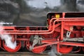 Old red driving wheels of a steam locomotive engine with steam