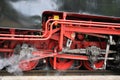 Old red driving wheels of a steam locomotive engine with steam