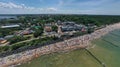 Drone aerial perspective and panoramic view on sunny beach with sunbathers with windbreaks and towels at sea in touristic city