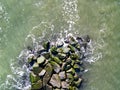 Drone aerial view directly over a rock jetty with ocean water pounding thee boulders