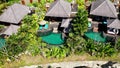 Drone aerial view of luxury hotel with straw roof villas and pools in tropical jungle and palm trees. Luxurious villa