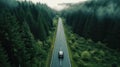 A drone captures a car driving along a highway nestled within a forest