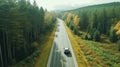 A drone captures a car driving along a highway nestled within a forest