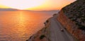 DRONE: Flying behind tourist car driving down empty road leading around island. Royalty Free Stock Photo