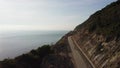 Drone following a motorbiker driving along on a curvy coastal empty road.