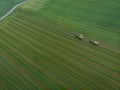 Drone shot of agricultural field with tractors harvesting hay