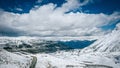 Drone shot of the cars on an asphalt snowy mountains road under blue cloudy sky