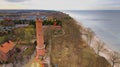 A drone captures Gaski beach, West Pomeranian Voivodeship, Poland, featuring a red brick lighthouse, Baltic Sea, sandy shore,