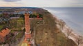 A drone captures Gaski beach, West Pomeranian Voivodeship, Poland, featuring a red brick lighthouse, Baltic Sea, sandy shore,