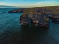 Drone shot of naturally formatted rocky cliffs in the sea under blue cloudy sky at sunset Royalty Free Stock Photo