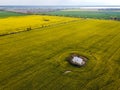 Drone shot of rape field with a pond in the forground and the horizon in the background