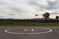 Drone taking off from a small helicopter landing base against cloudy sky