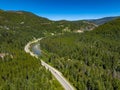 Drone view of Crowsnest Highway by river passing through rocks, dense forests and mountains, Canada.