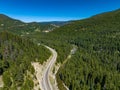 Drone view of Crowsnest Highway by river passing through rocks, dense forests and mountains, Canada.