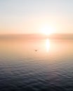 Drone view of golden sky above calm sea at sunset with the silhouette of person rowing a boat